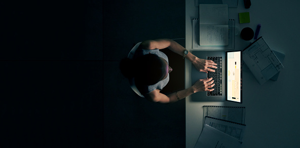High angle shot of a young businesswoman using a laptop during a late night in a modern office