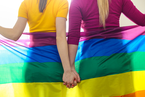 Unrecognizable Lesbian couple with a rainbow flag, holding hands.
