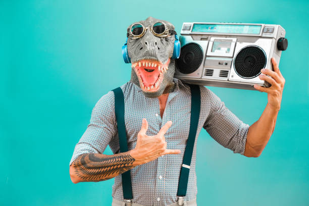 Crazy senior man dancing rock music wearing t-rex mask - Tattoo trendy guy having fun listening music with boombox stereo - Absurd and funny trend concept - Focus on face Crazy senior man dancing rock music wearing t-rex mask - Tattoo trendy guy having fun listening music with boombox stereo - Absurd and funny trend concept - Focus on face mask disguise photos stock pictures, royalty-free photos & images