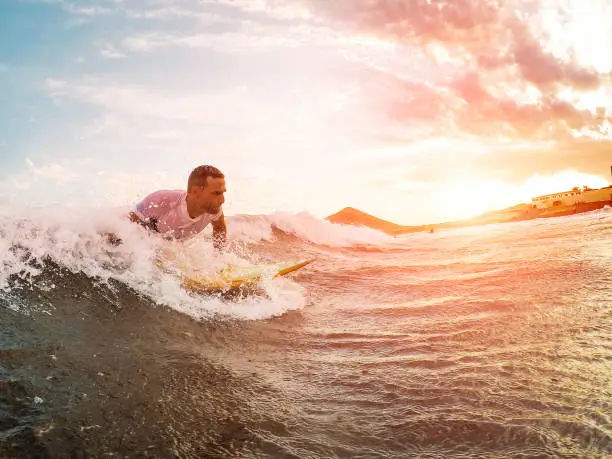 Photo of Male athlete surfing at sunset - Surfer man performing outdoor inside ocean- Extreme sport, competition, travel and summer vacation concept - Soft focus on man head