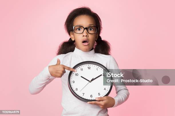 Surprised Africanamerican Girl Holding Big Clock And Pointing On It Stock Photo - Download Image Now