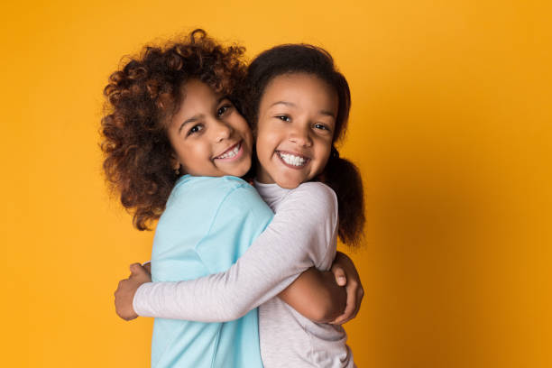 istock Girls hugging and laughing over yellow background 1135964982