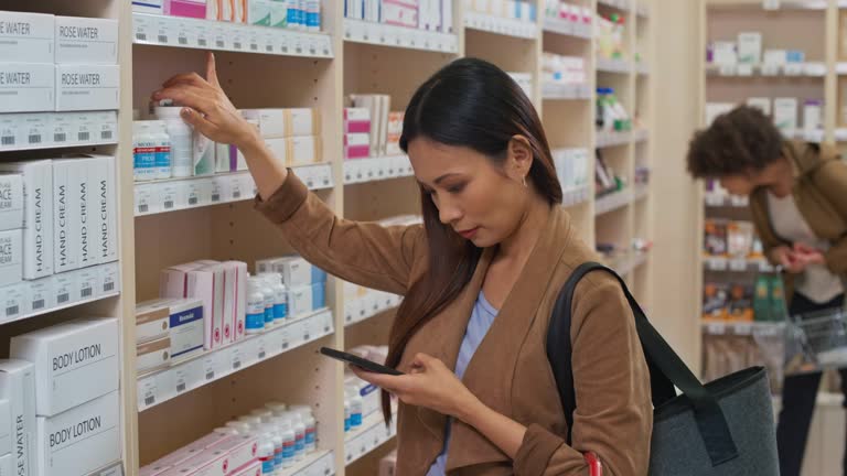 DS Asian woman checking her phone before taking a medicine bottle from the shelf at the drugstore