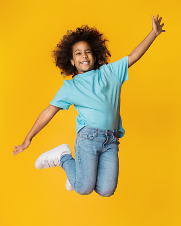 Little african-american girl jumping over yellow studio background