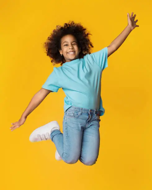 Little african-american girl jumping over yellow studio background