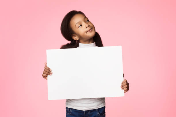 Little thoughtful girl holding blank board over background Little thoughtful girl holding blank board for your text over pink background kids using smart board stock pictures, royalty-free photos & images