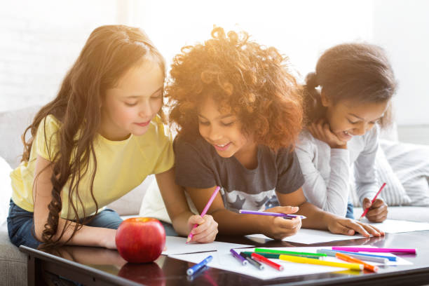 les filles multiethniques dessinant à la table avec des crayons colorés - early childhood education photos et images de collection