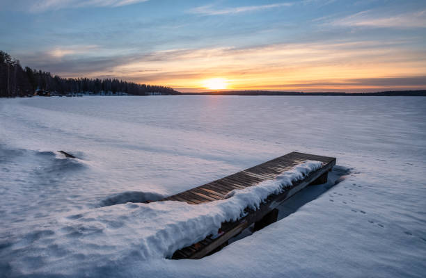 paysage hivernal pittoresque avec la jetée et le coucher du soleil à la lumière du soir en finlande - finland sauna lake house photos et images de collection