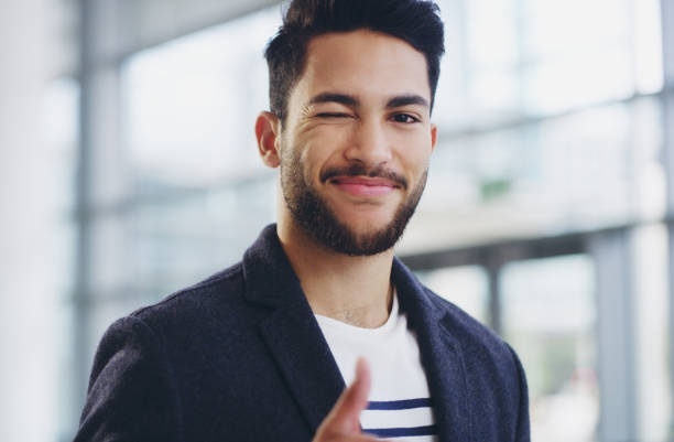 I've got this! Cropped shot of a young businessman showing winking and showing thumbs up while walking through a modern office young man wink stock pictures, royalty-free photos & images