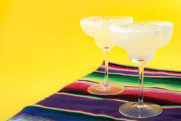 Happy Cinco de Mayo, Mexico fiesta and cocktail party concept theme with two margaritas and a Mexican stripped pattern rug named serape isolated on yellow background with copyspace Happy Cinco de Mayo, Mexico fiesta and cocktail party concept theme with two margaritas and a Mexican stripped pattern rug named serape isolated on yellow background with copy space tequila drink photos stock pictures, royalty-free photos & images