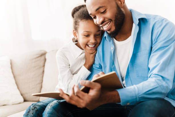 little girl and father enjoying reading book together - family reading african descent book imagens e fotografias de stock