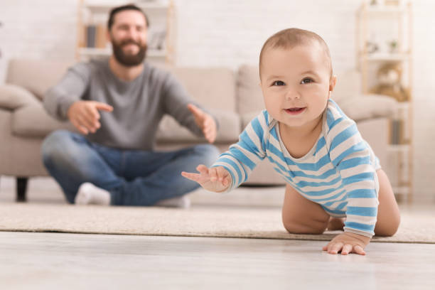 Adorable baby boy crawling on floor with dad Play with me. Adorable baby boy crawling on floor at home, daddy watching his son, copy space crawling photos stock pictures, royalty-free photos & images
