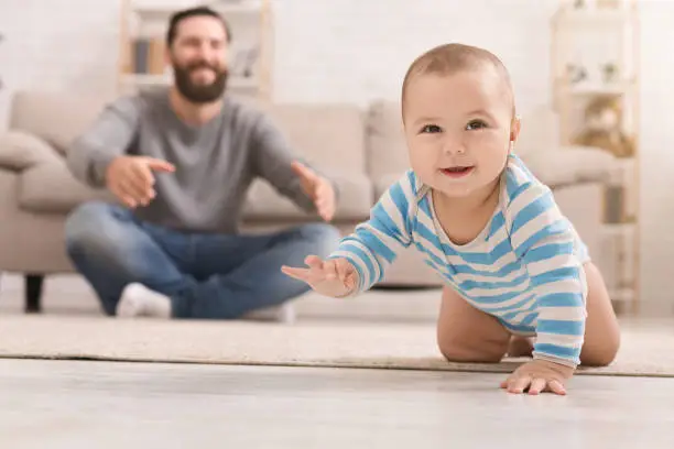 Play with me. Adorable baby boy crawling on floor at home, daddy watching his son, copy space