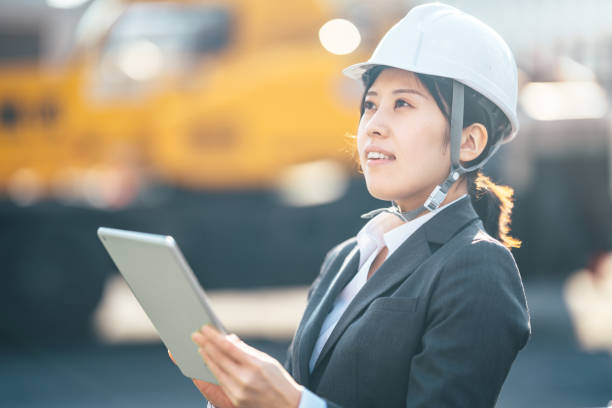 молодая женщина с помощью цифрового планшета на строительной площадке - manual worker portrait helmet technology стоковые фото и изображения