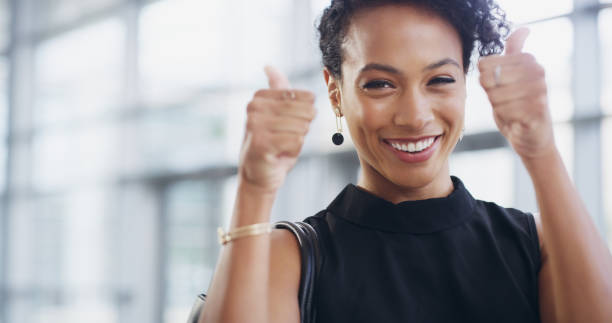 Business will always have my backing Cropped shot of a young businesswoman showing thumbs up while walking through a modern office thank you phrase stock pictures, royalty-free photos & images