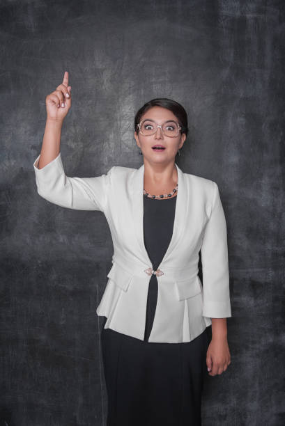 istock Smiling funny teacher showing up by finger on blackboard 1135980053