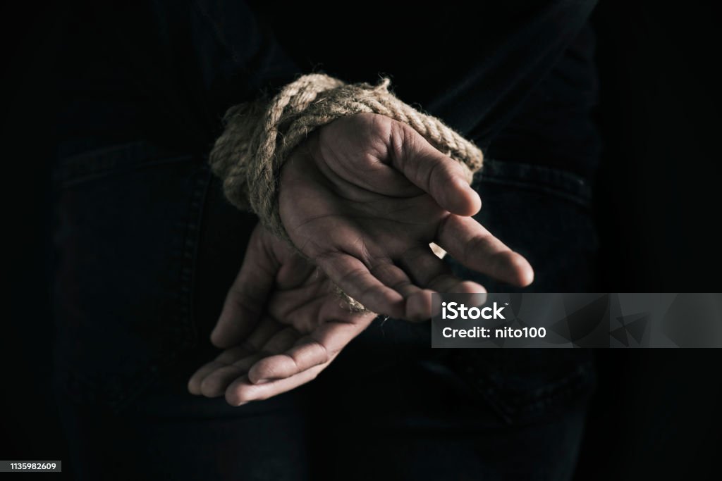 man with his hands tied behind his back closeup rear view of a man with his hands tied behind his back with rope, against a black background Kidnapping Stock Photo