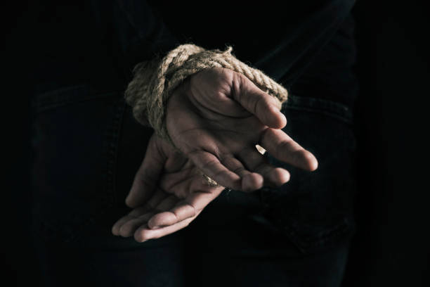 man with his hands tied behind his back closeup rear view of a man with his hands tied behind his back with rope, against a black background tied up stock pictures, royalty-free photos & images