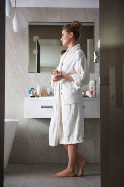 istock Young smiling lady in bathroom holding face cream 1135983058