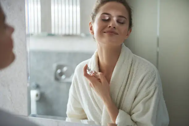 Photo of Young smiling lady enjoying her perfume in morning