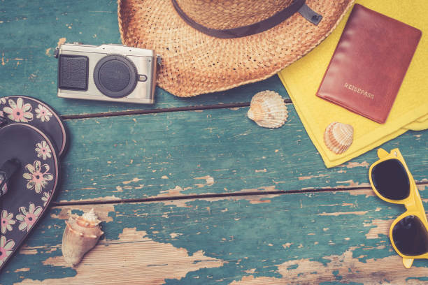 istock Holiday Concept: Vintage wood table with holiday accessories: Straw hat, sunglasses, shells, vintage camera, passport and flip flops. Text space. 1135984113