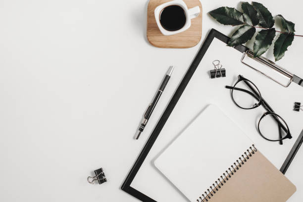 istock Home office workspace mockup with blank clip board, office supplies, pen, green leaf, coffee cup on a wooden stand and eyeglasses on white background. Flat lay, top view, copy space 1135986113