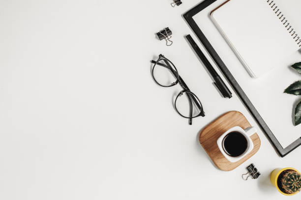 istock Flat lay office workspace with blank clip board, office supplies, pen, cactus, green leaf, coffee cup on a wooden stand and eyeglasses on white background. Top view minimal mock up template concept 1135986600