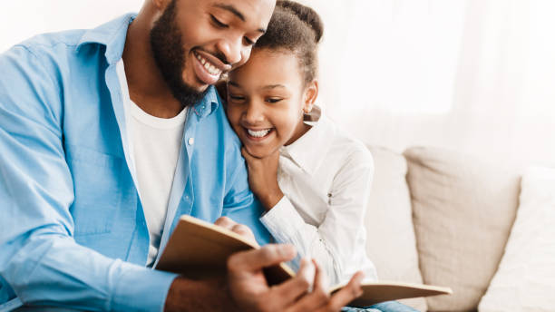 père et descendant lisant le livre ensemble à la maison - family reading african descent book photos et images de collection