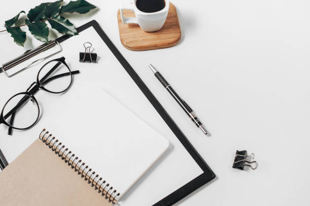 istock Home office workspace mockup with blank clip board, office supplies, pen, green leaf, coffee cup on a wooden stand and eyeglasses on white background. Flat lay, top view, copy space 1135987591