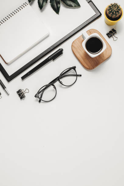 istock Flat lay office workspace with blank clip board, office supplies, pen, cactus, green leaf, coffee cup on a wooden stand and eyeglasses on white background. Top view minimal mock up template concept 1135987592