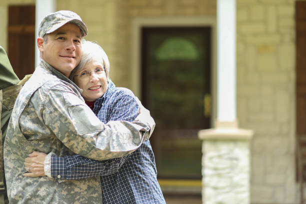 Family welcomes home USA army soldier. Family welcomes home a USA army soldier. Mother excitedly hugs adult son, who wears combat uniform and carries duffle bag. They stand in front of mother's home. proud army mom stock pictures, royalty-free photos & images