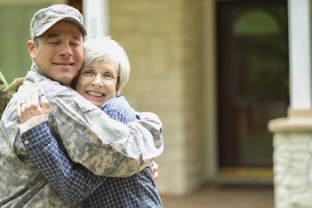 Family welcomes home USA army soldier. Family welcomes home a USA army soldier. Mother excitedly hugs adult son, who wears combat uniform and carries duffle bag. They stand in front of mother's home. proud army mom stock pictures, royalty-free photos & images