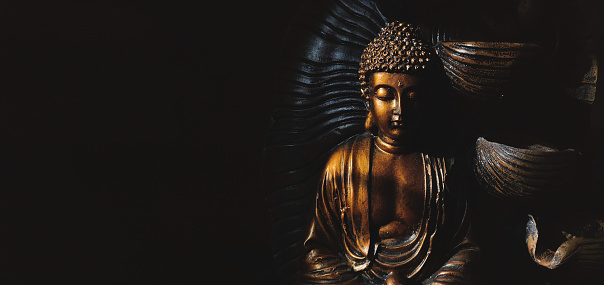 Golden Gautama Buddha statue with a black background depicting darkness and hope.