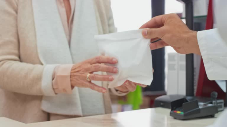 Hands of a pharmacists placing the prescription medicine into a white bag and handing it to the customer