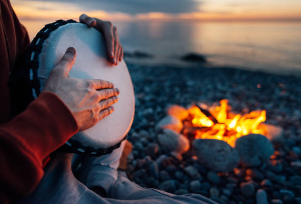 istock percussionist plays djembe on the seashore near fire, hands close up 1135994866