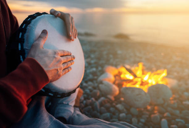 istock percussionist plays djembe on the seashore near fire, hands close up 1135995839
