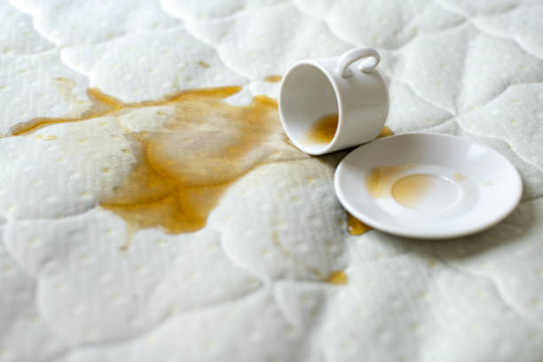 Spilled cup of tea on the bed. Accidentally dropped cup with saucer on white bedsheet. Unlucky, unfortunate breakfast. Wet spot. stock photo