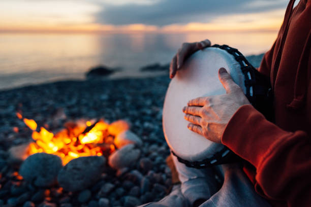 percussionist plays djembe on the seashore near fire, hands close up