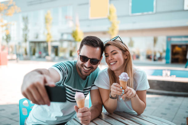 Good looking young man with sunglasses taking selfie with his girlfriend while they eating ice cream stock photo
