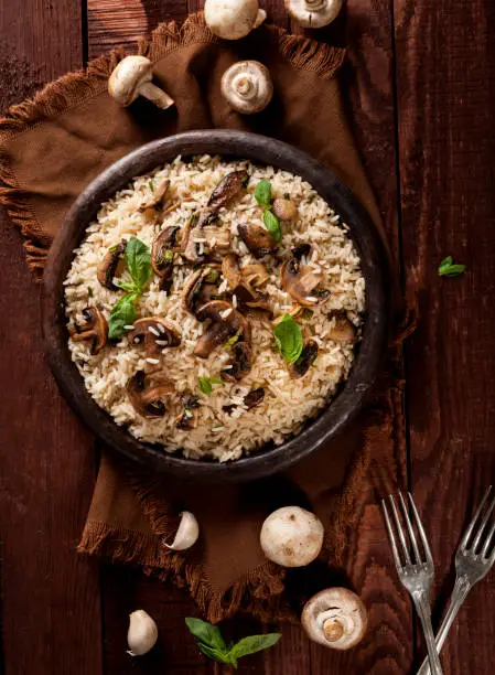 Cooked white rice with mushrooms in a bowl on wooden background. Top view with copy space.