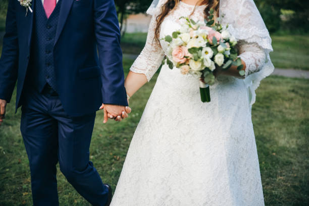 hochzeitspaar spaziert im grünen park curvy braut in weißem spitzenkleid und bräutigam halten die hände. übergewichtige glückliche menschen. liebesgeschichte im freien. schöner strauß. - veil bride lace married stock-fotos und bilder