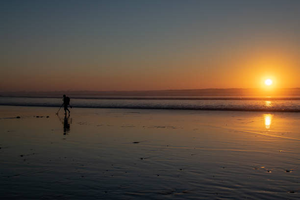istock Using a metal detector to search for hidden treasure on a beach at sunset 1136008899