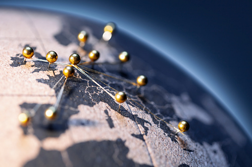States and capitals of the European Union pinned with golden pins on a cork globe. The pins are connected to each other with a golden thread.