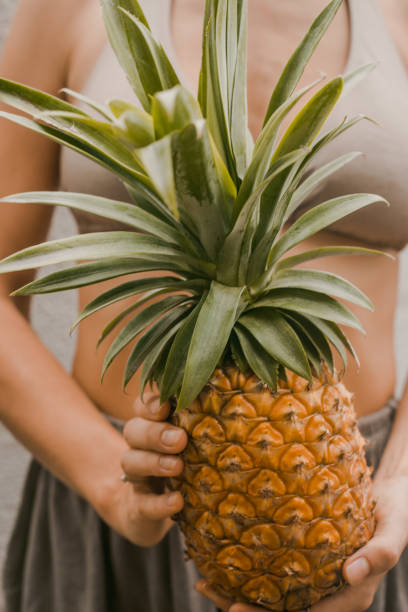istock woman in boho clothes keep the tropical fruit pineapple in hands on the light background in Bali 1136009853