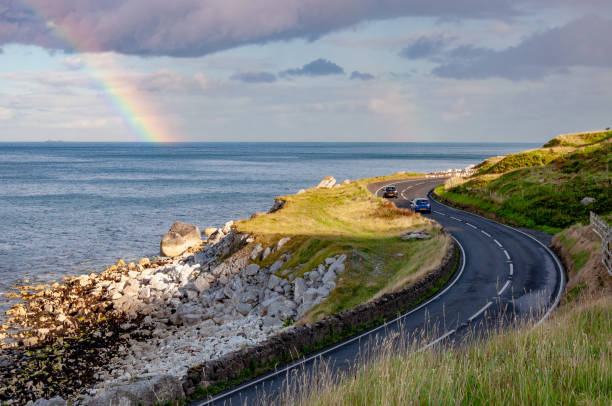 antrim coastal road y rainbow en irlanda del norte, reino unido - curve driving winding road landscape fotografías e imágenes de stock