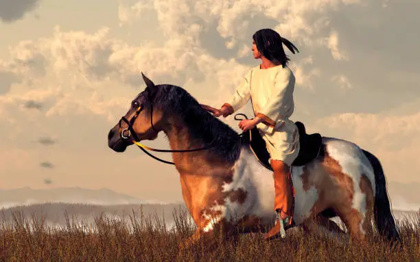 A Native American man rides his pinto through long grass in the plains of the American Wild West.  Off in the distance, smoke signals rise from low hills. 3D Rendering