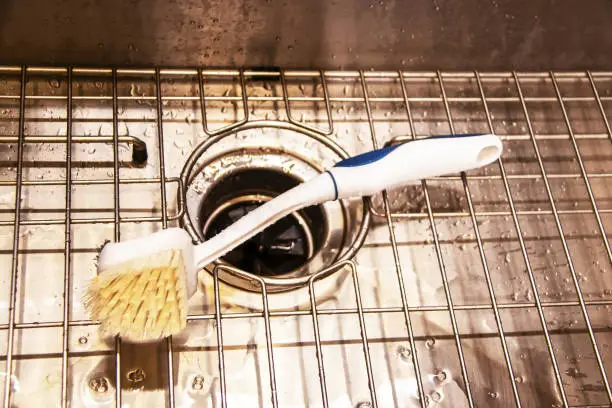 Photo of Wet stainless steel sink with garbage disposal and wire rack with scrub brush laying on it