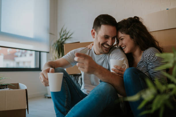 Young happy couple moving in new home and unpacking boxes. They are smiling and drinking a coffee. stock photo
