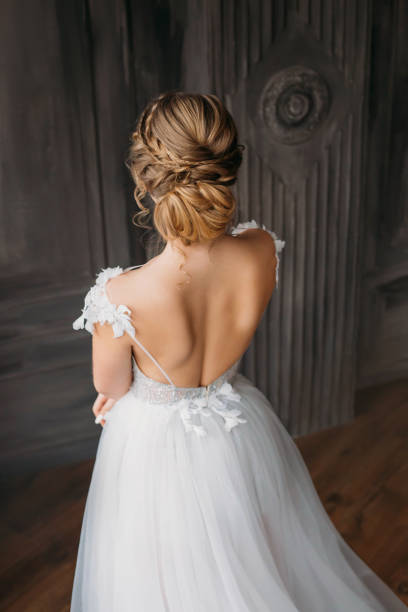 hairstyle for blond long hair, advertising announcement of beauty salon for wedding and prom 2019, image of graduate in white expensive adorable dress with open back, lade in a spacious room hairstyle for blond long hair, advertising announcement of beauty salon for wedding and prom 2019, image of graduate in white expensive adorable dress with open back, lade in a spacious room. evening gown photos stock pictures, royalty-free photos & images