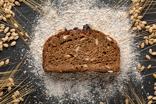 Slice of wholegrain bread with flour and cereal plant photographed close up on black background